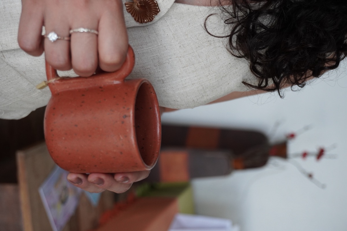Mão segurando uma caneca de cerâmica terracota