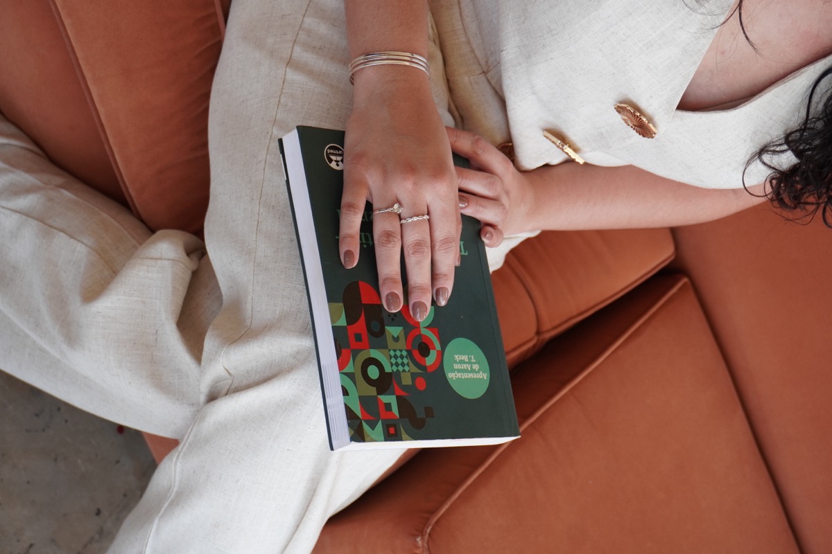 Mãos sobre um livro, sentada em um sofá terracota